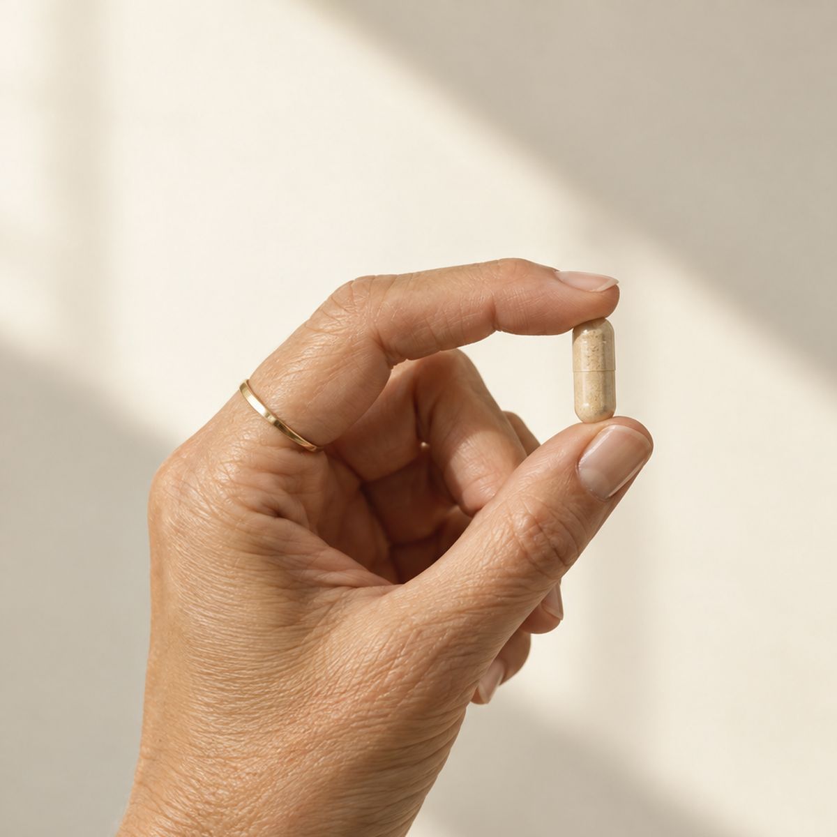Eine Hand hält eine einzelne beige Kapsel zwischen Daumen und Zeigefinger im Sonnenlicht
