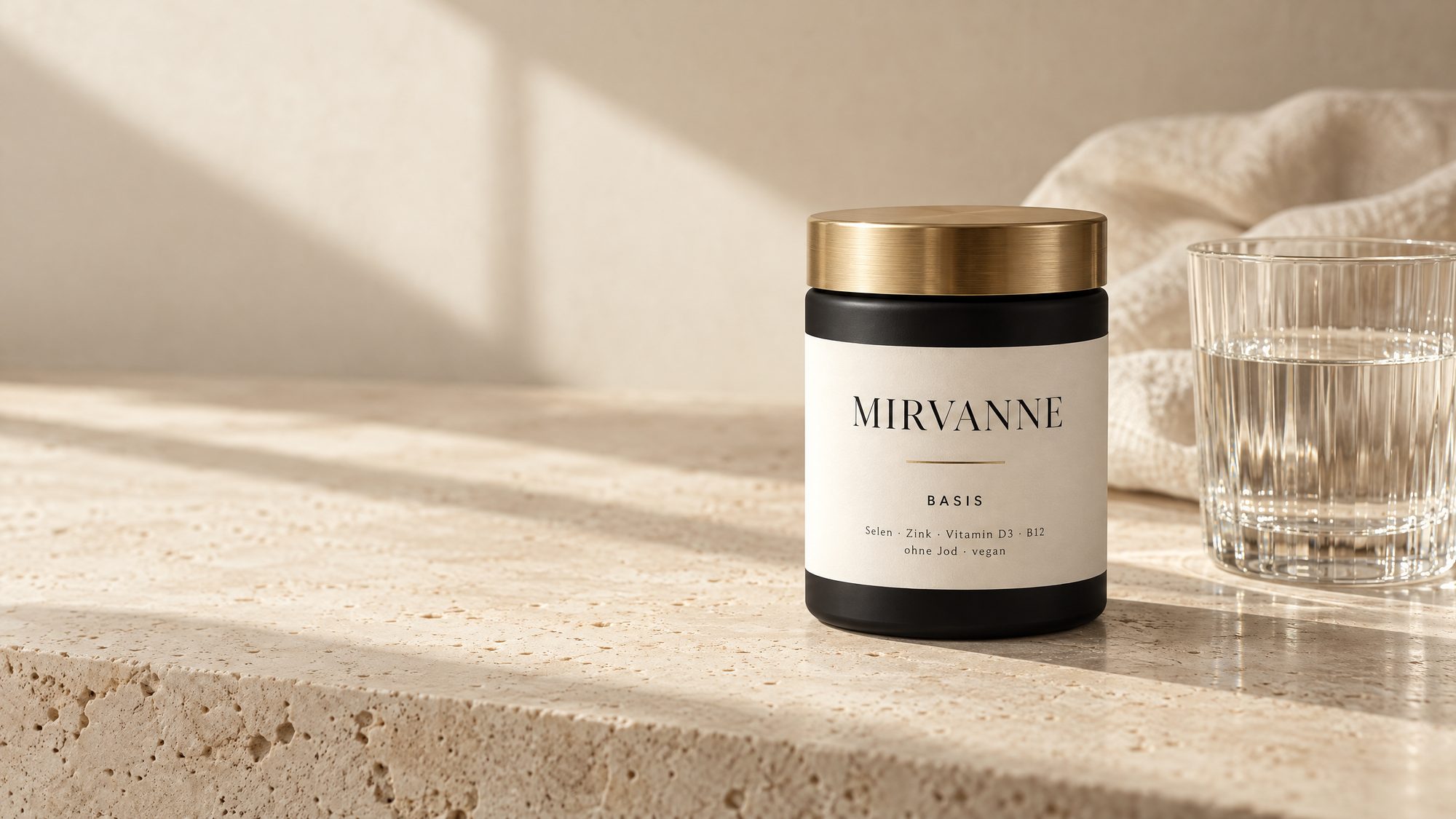 Mirvanne Basis: schwarze Dose mit goldenem Deckel auf hellem Travertin, daneben ein Glas Wasser im Mittagslicht